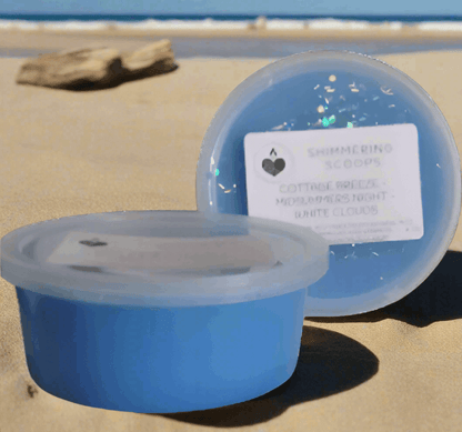 Two blue scoopable wax tarts on a sandy beach with ocean in the background, labeled 'Shimmering Scoops'.